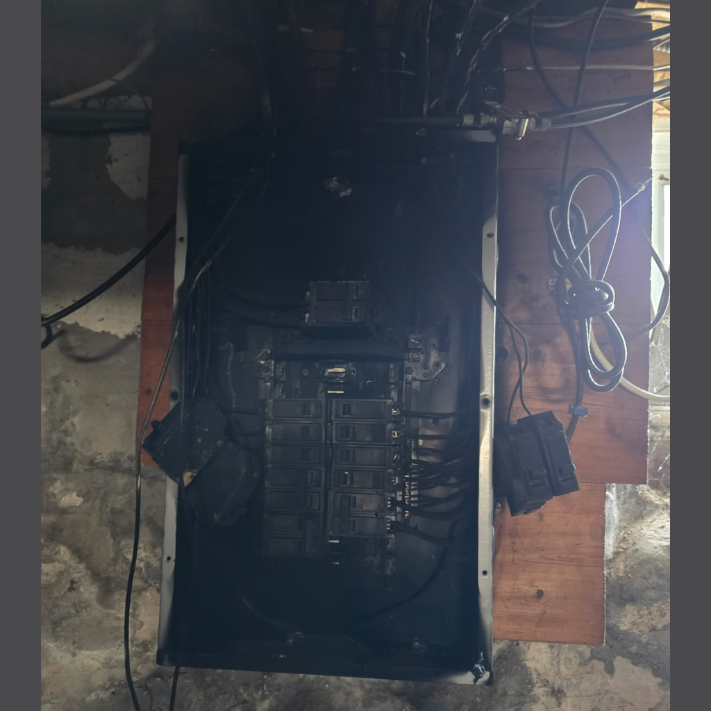 Open electrical panel with visible heat damage around breakers and electrical wiring