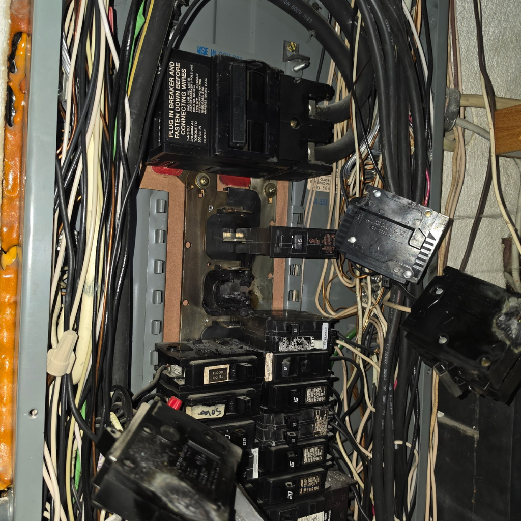 Open electrical panel with damaged breakers, wiring, and signs of overheating